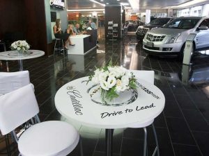 עיצוב אולם תצוגה לרכבי קדילאק עם עמדות אירוח אלגנטיות, שולחנות מעוצבים ופרחים לבנים