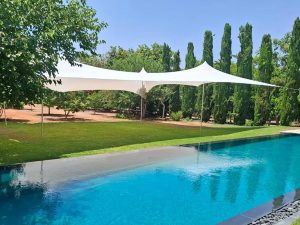 בריכת שחייה עם דשא ירוק ופרגולת הצללה לבנה בגינה פרטית