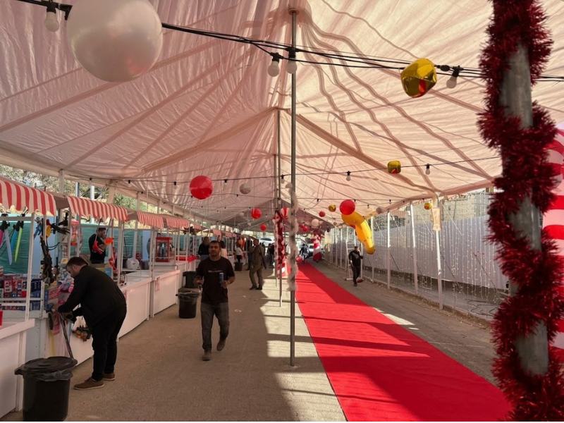 מבט מתוך אוהל מקורה על שדרת ביתנים עם דוכנים בצבעי אדום ולבן משמאל